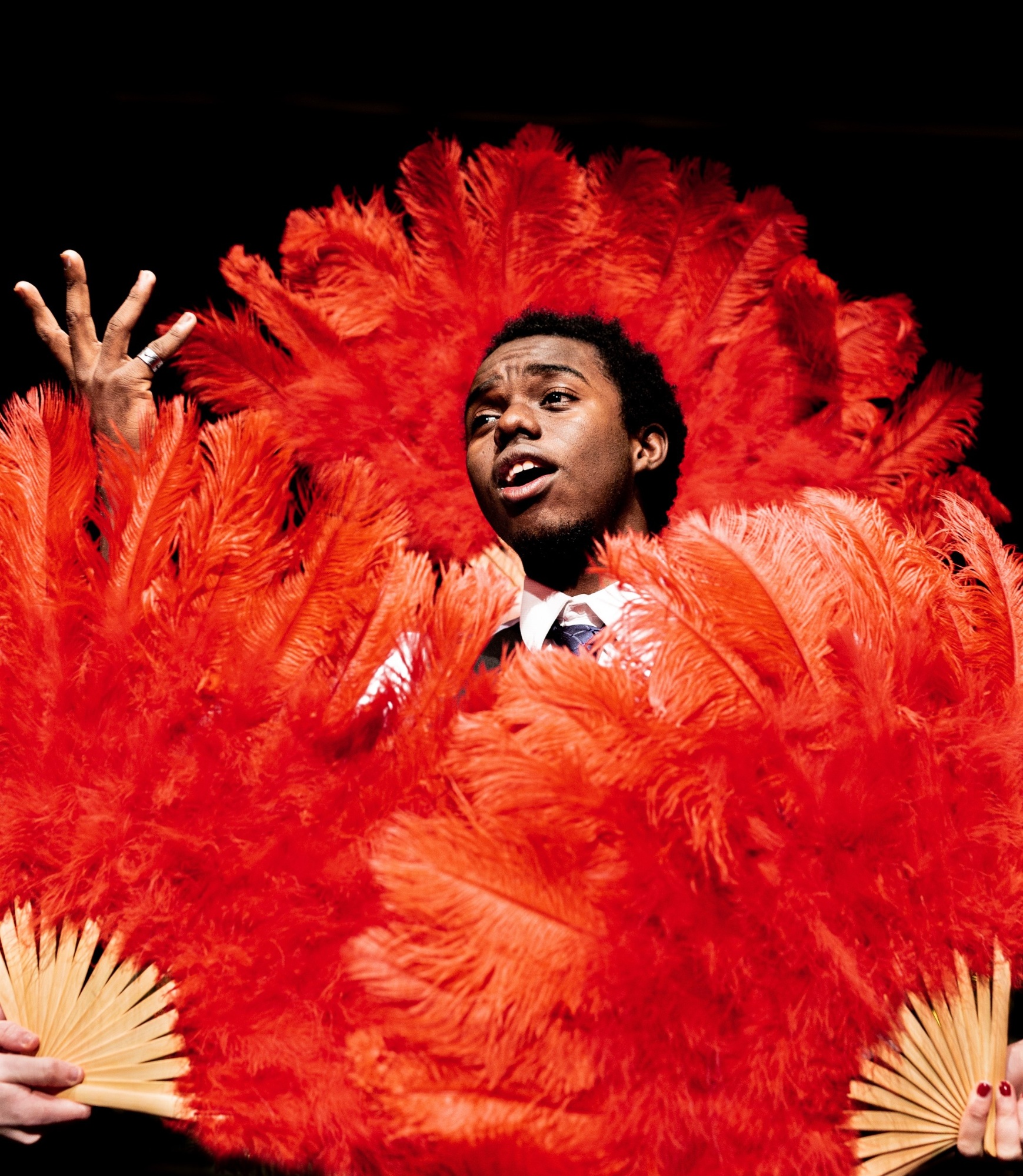 male student singing, surrounded by red feather fans