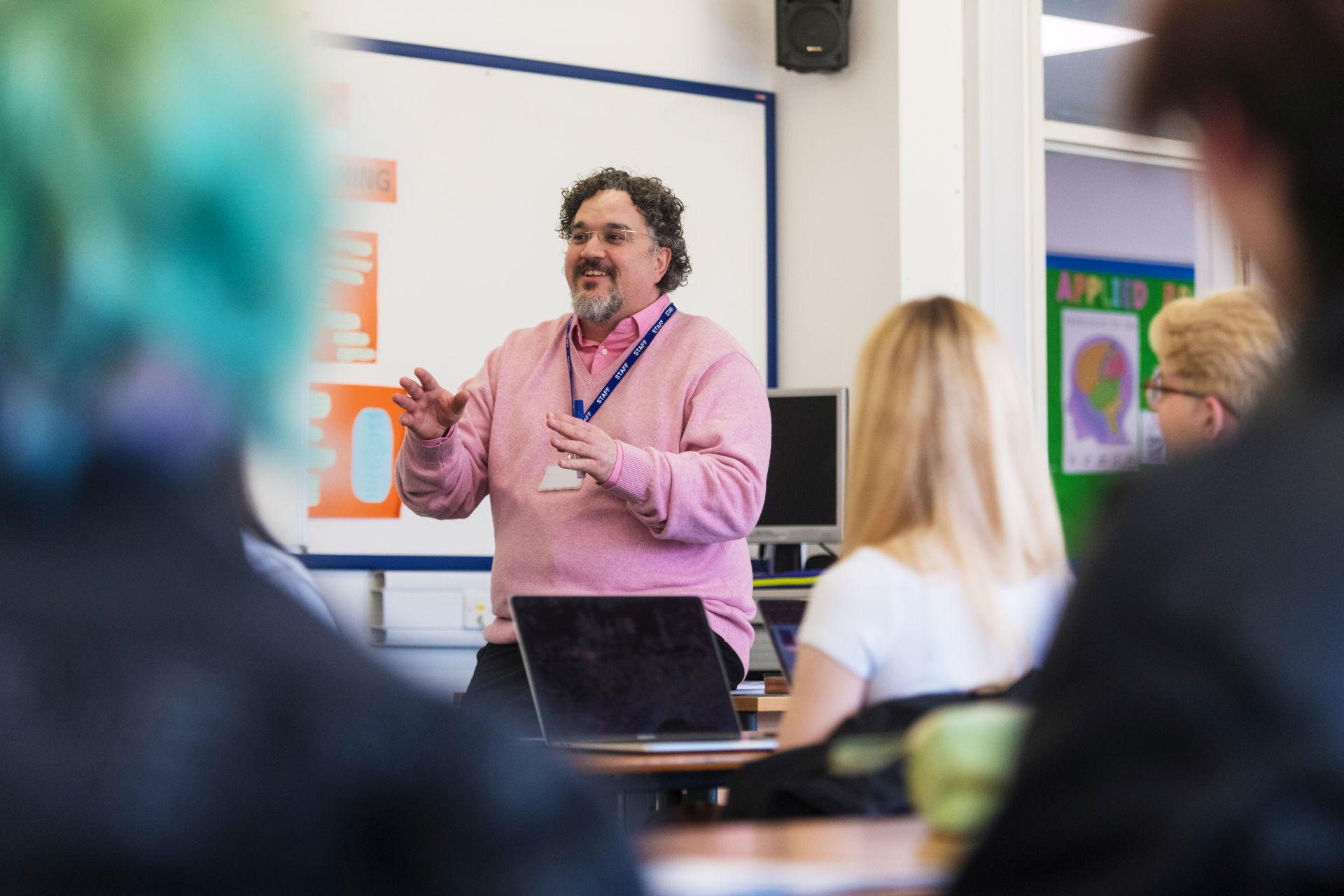 male teacher stood in front of a whiteboard talking to a class a students