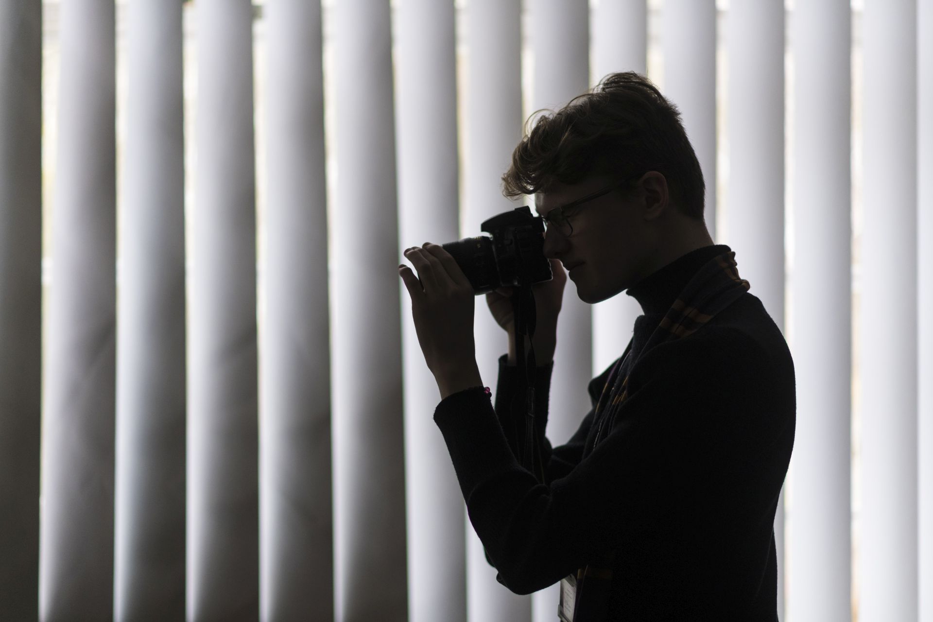 male student in silhouette holding a camera to his face