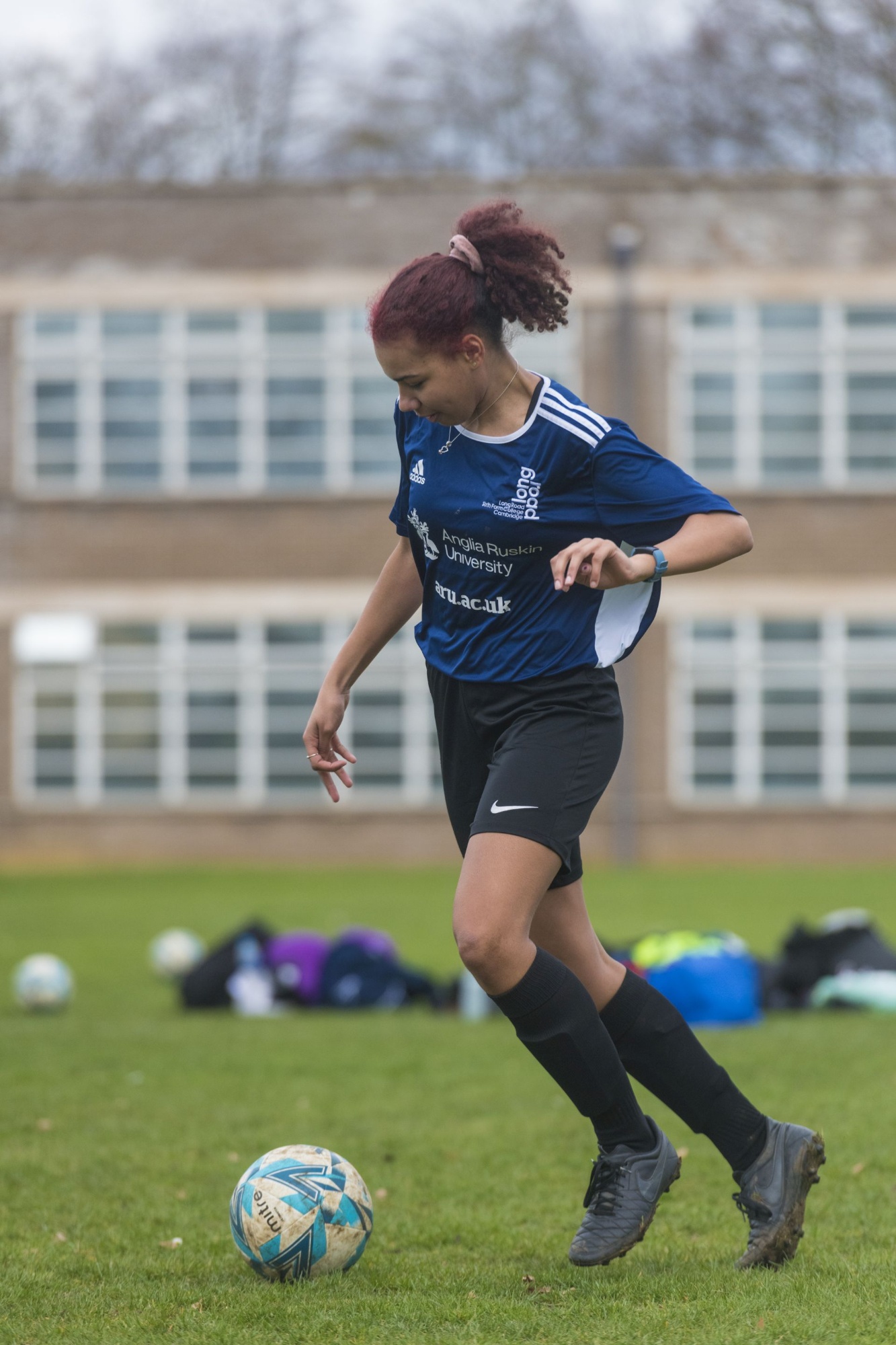 female student in blue sports kit playing football