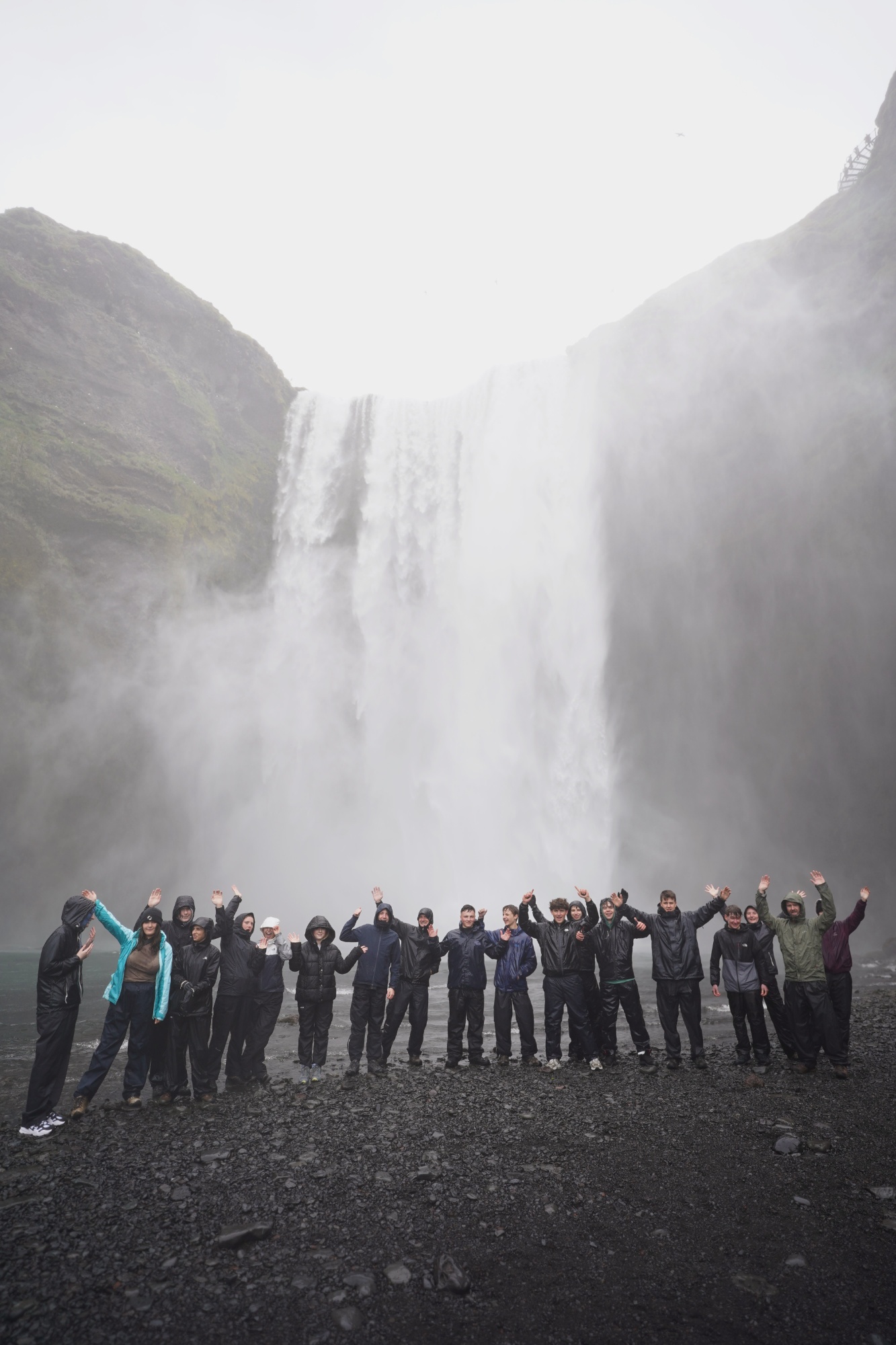 Group of male and female students wearing waterproof clothing stood at the bottom of a large waterfall in Iceland
