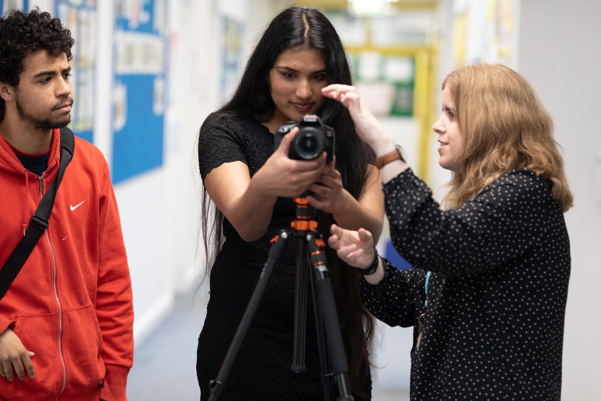 male and female student working with female teacher, using a small filming camera on a tripod stand