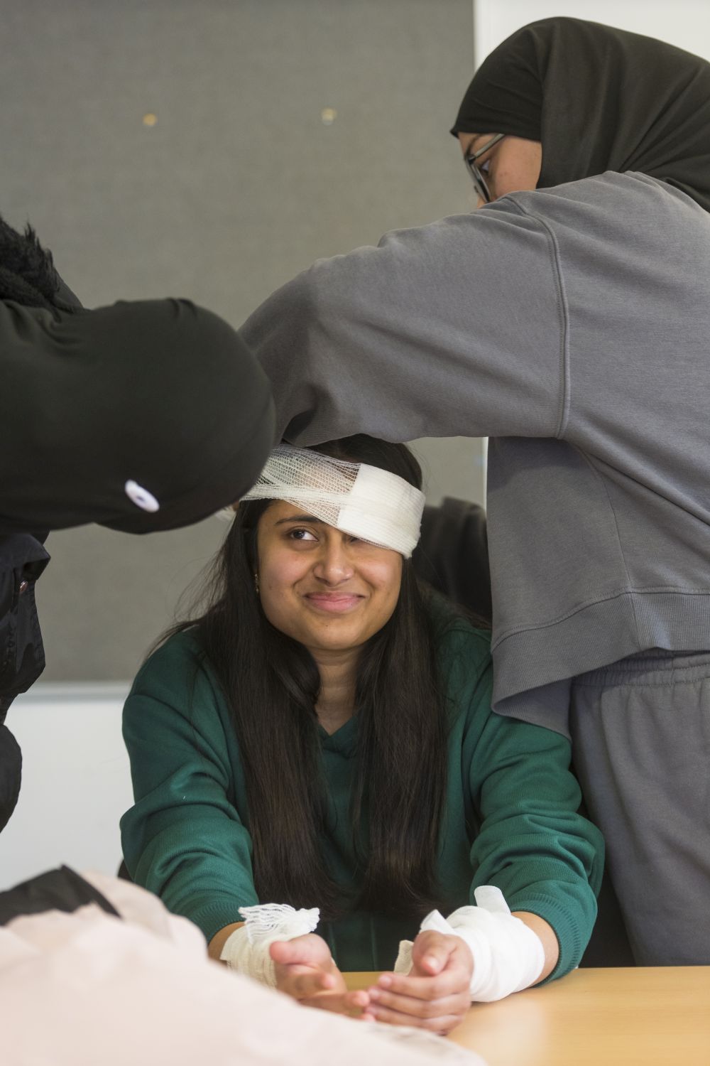 two female students working together to practice applying bandages on a third female student