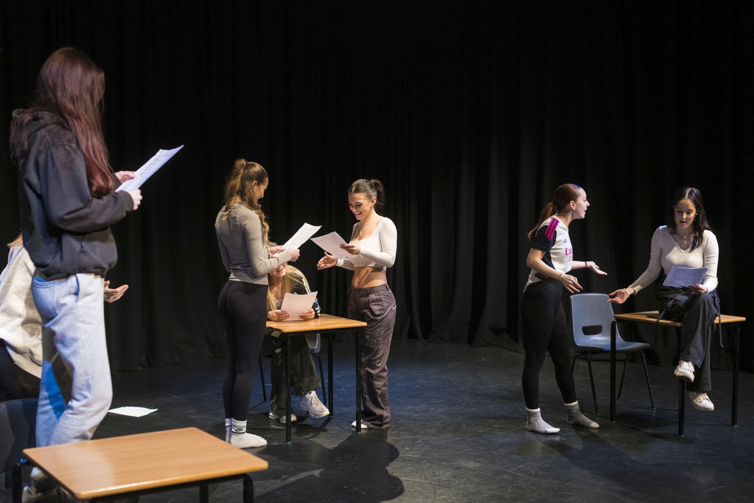 group of female students spread across a black box theatre in pairs, reading from scripts